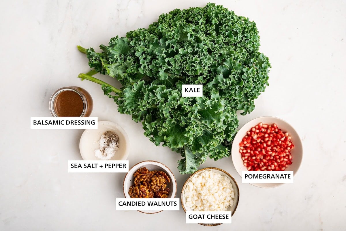 Ingredients measured out to make Christmas Salad: kale, pomegranate, goat cheese, candied walnuts, sea salt, pepper and balsamic dressing.