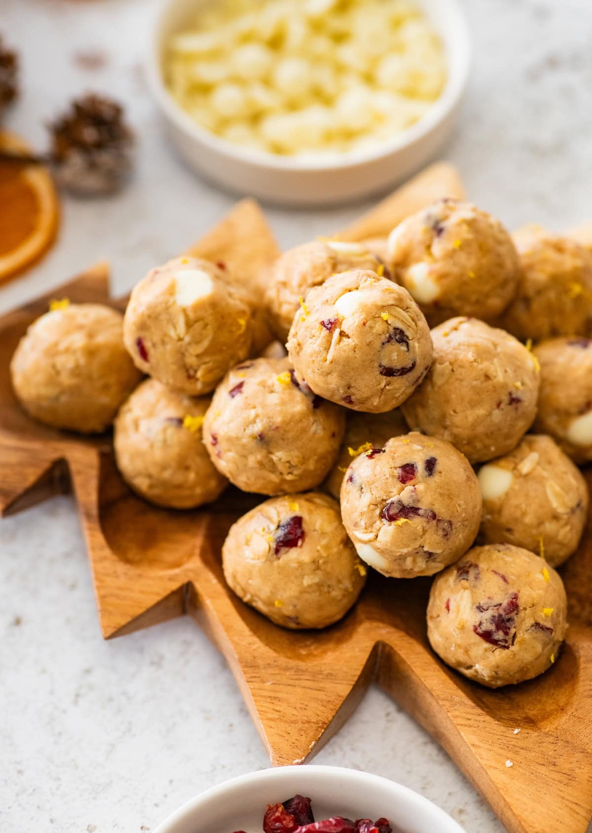 A wooden tray shaped like a pine tree holding a stack of cranberry orange protein balls.