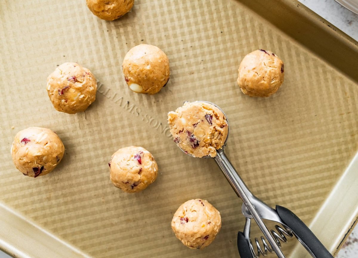 A cookie scoop portioning out cranberry orange protein balls onto a baking tray.