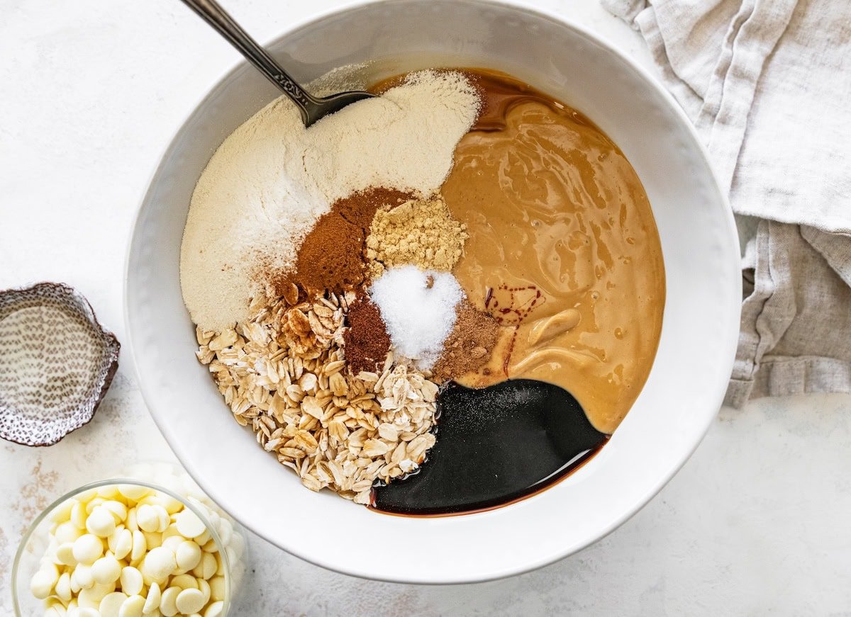 Mixing bowl filled with oats, spices, molasses, protein powder and cashew butter before stirring.