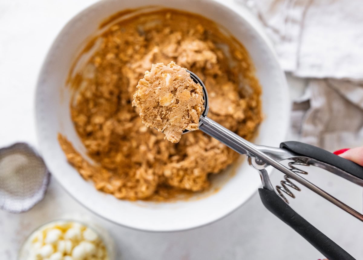 Cookie scoop lifting gingerbread protein ball mixture from a mixing bowl before rolling into balls.