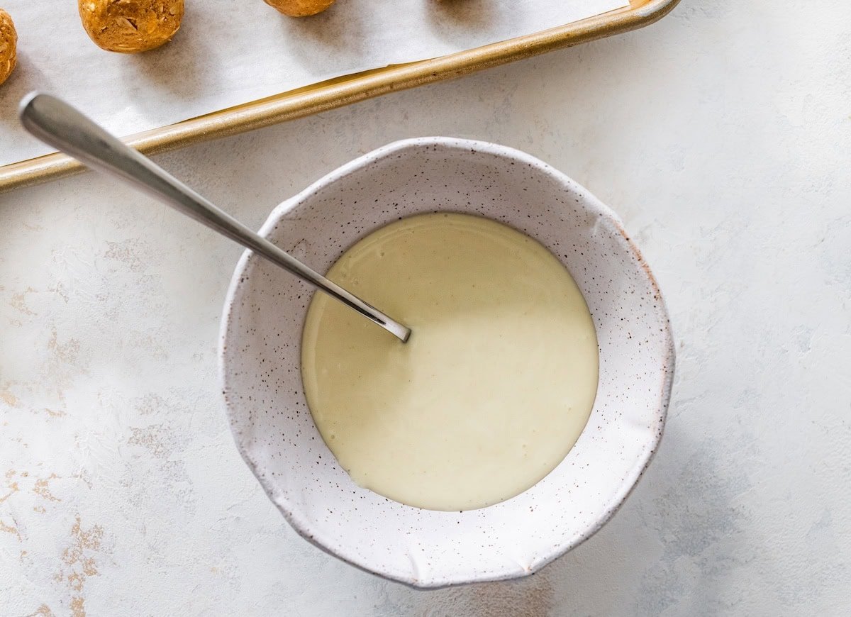 Bowl of melted white chocolate with a spoon, ready for drizzling over gingerbread protein balls.