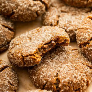 Multiple gingersnap cookies near one another on parchment paper, with one cookie having a bite taken from it.