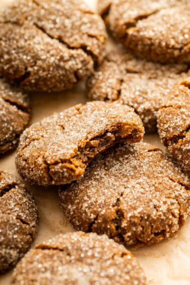 Multiple gingersnap cookies near one another on parchment paper, with one cookie having a bite taken from it.