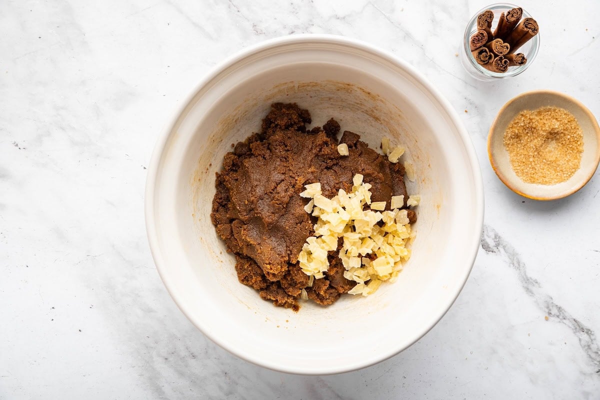 Gingersnap cookie dough in a medium mixing bowl with crystalized ginger added to it.