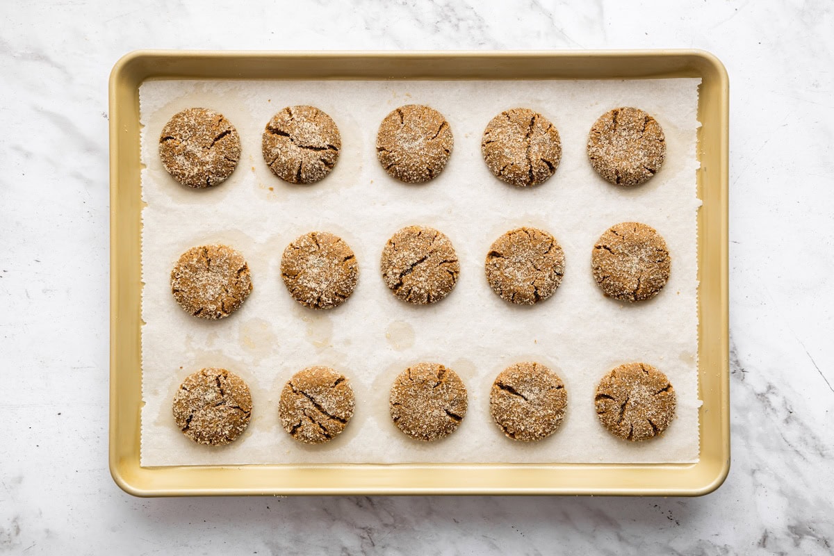 Gingersnap cookies coated in cane sugar on a baking sheet after being baked.