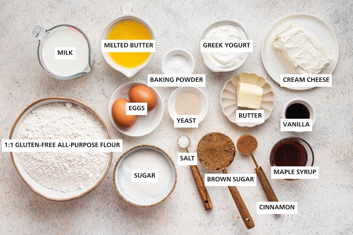 Ingredients measured out to make Gluten-Free Cinnamon Rolls: 1:1 all purpose gluten-free flour, milk, sugar, eggs, melted butter, salt, yeast, baking powder, brown sugar, Greek yogurt, butter, cinnamon, maple syrup, vanilla and cream cheese.