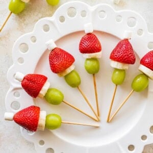 Plate of Grinch fruit kabobs showing strawberries, banana slices, grapes and mini marshmallows.