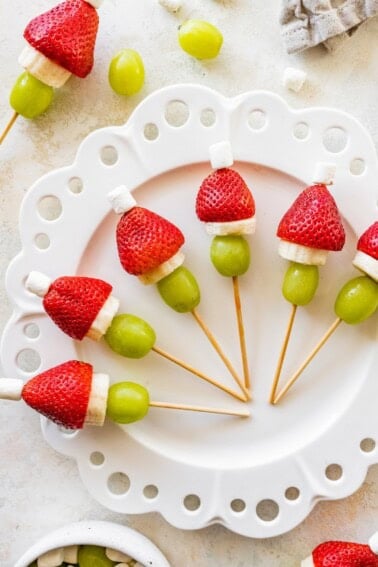 Plate of Grinch fruit kabobs showing strawberries, banana slices, grapes and mini marshmallows.