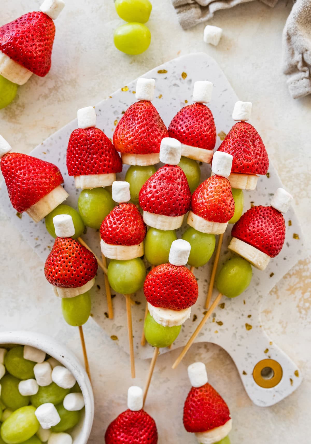 Grinch fruit kabobs arranged on a platter with strawberries, bananas, grapes and marshmallows.