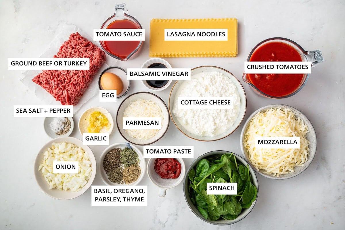 Ingredients measured out to make Healthy Lasagna: sea salt, pepper, onion, ground beef, garlic, basil, oregano, parsley, thyme, tomato sauce, parmesan, egg, tomato paste, balsamic vinegar, cottage cheese, lasagna noodles, spinach, mozzarella and crushed tomatoes.