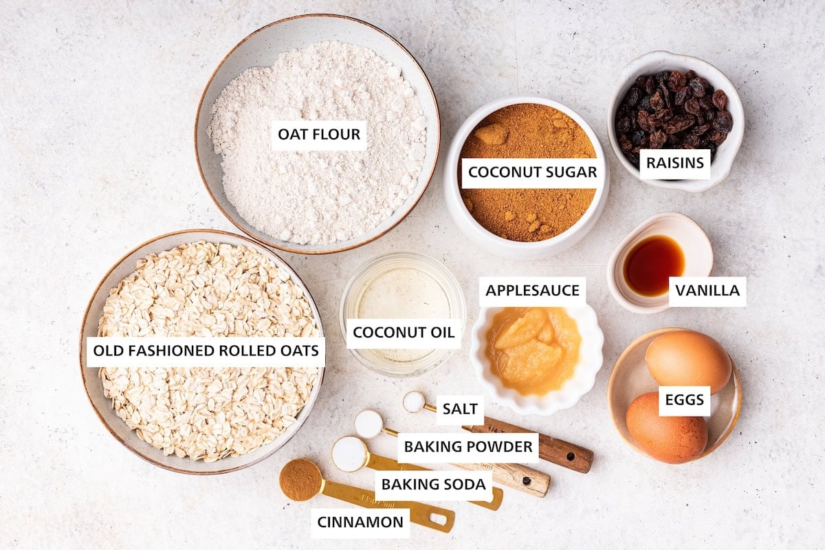 Ingredients measured out to make Oatmeal Raisin Cookies: oats, oat flour, cinnamon, baking soda, baking powder, coconut oil, sea salt, applesauce, coconut sugar, eggs, vanilla and raisins.