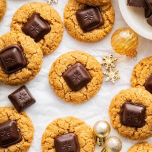 Peanut butter blossom cookies arranged on white parchment with small gold ornaments, and extra chocolate pieces scattered around.