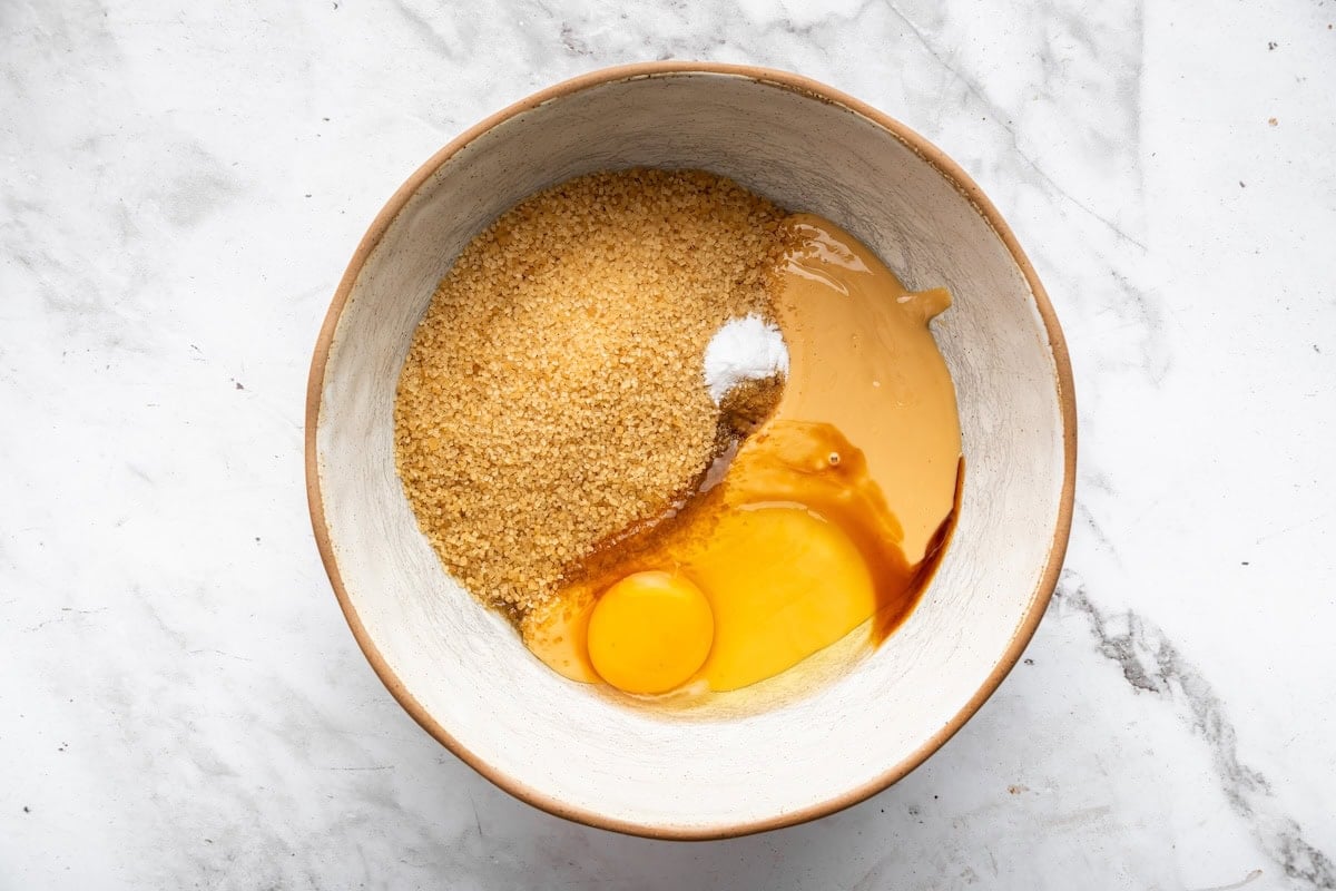 A ceramic mixing bowl filled with the base ingredients for peanut butter blossoms, all sitting unmixed and visible as separate components.
