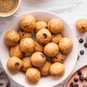 Bowl filled with peanut butter protein balls surrounded by scattered chocolate chips.
