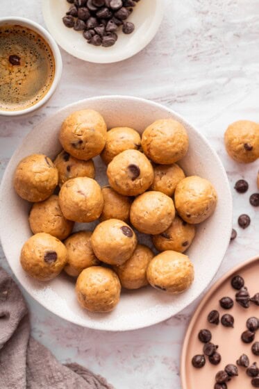 Bowl filled with peanut butter protein balls surrounded by scattered chocolate chips.