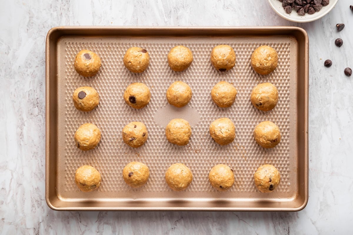 Tray of rolled peanut butter protein balls spaced evenly on a baking sheet.