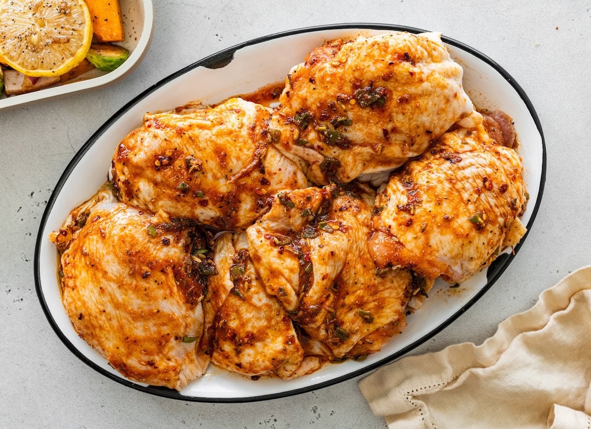 Raw chicken thighs coated in sauce Raw chicken thighs coated in sauce on a white serving dish before baking.