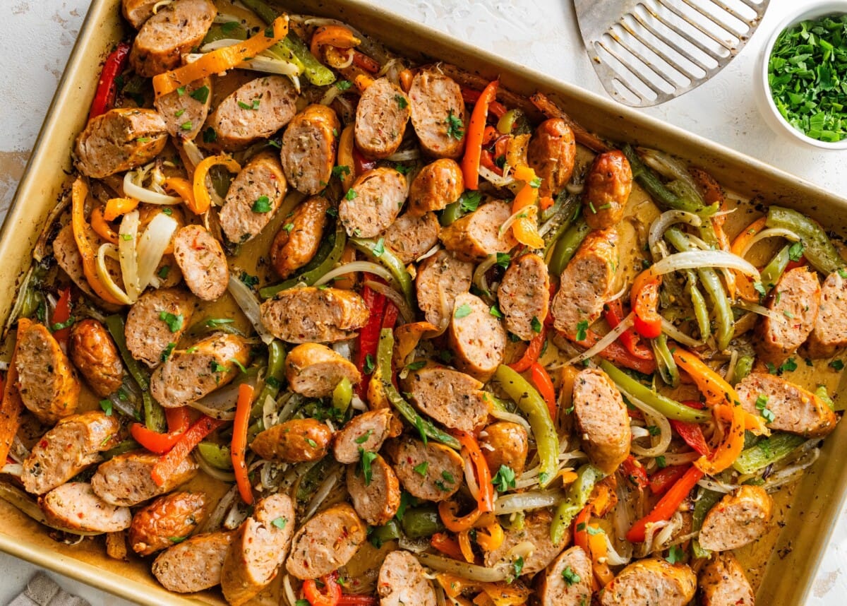 Sheet pan of sliced chicken sausage with roasted peppers and onions garnished with parsley.