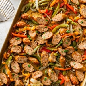 Close up sheet pan with sliced chicken sausage, roasted peppers and caramelized onions.