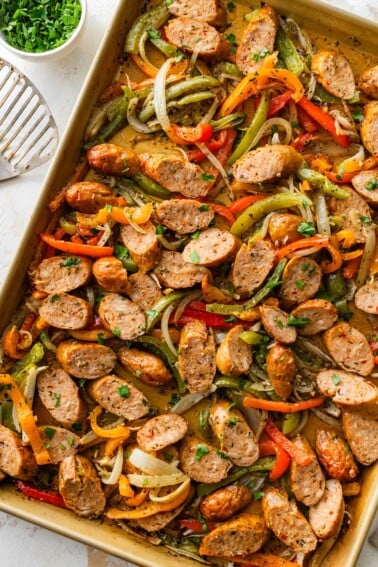 Close up sheet pan with sliced chicken sausage, roasted peppers and caramelized onions.