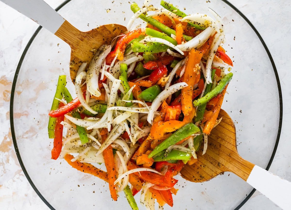 Bowl of sliced peppers and onions tossed with olive oil and seasonings.
