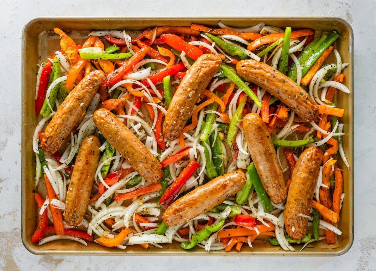Sheet pan with chicken sausage, peppers and onions arranged before roasting.