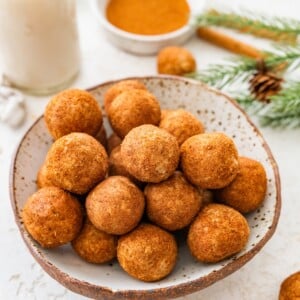 Bowl of snickerdoodle protein balls coated in cinnamon sugar with holiday greenery in back.