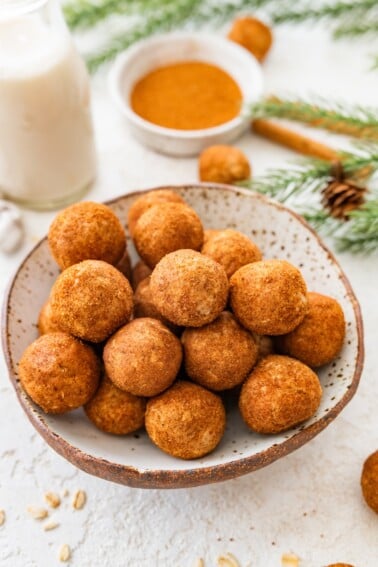 Bowl of snickerdoodle protein balls coated in cinnamon sugar with holiday greenery in back.