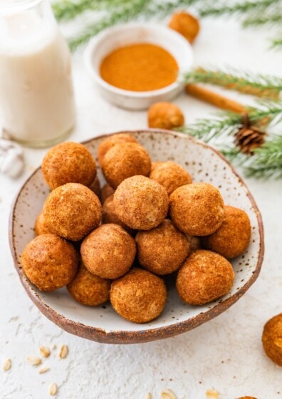Bowl of snickerdoodle protein balls coated in cinnamon sugar with holiday greenery in back.