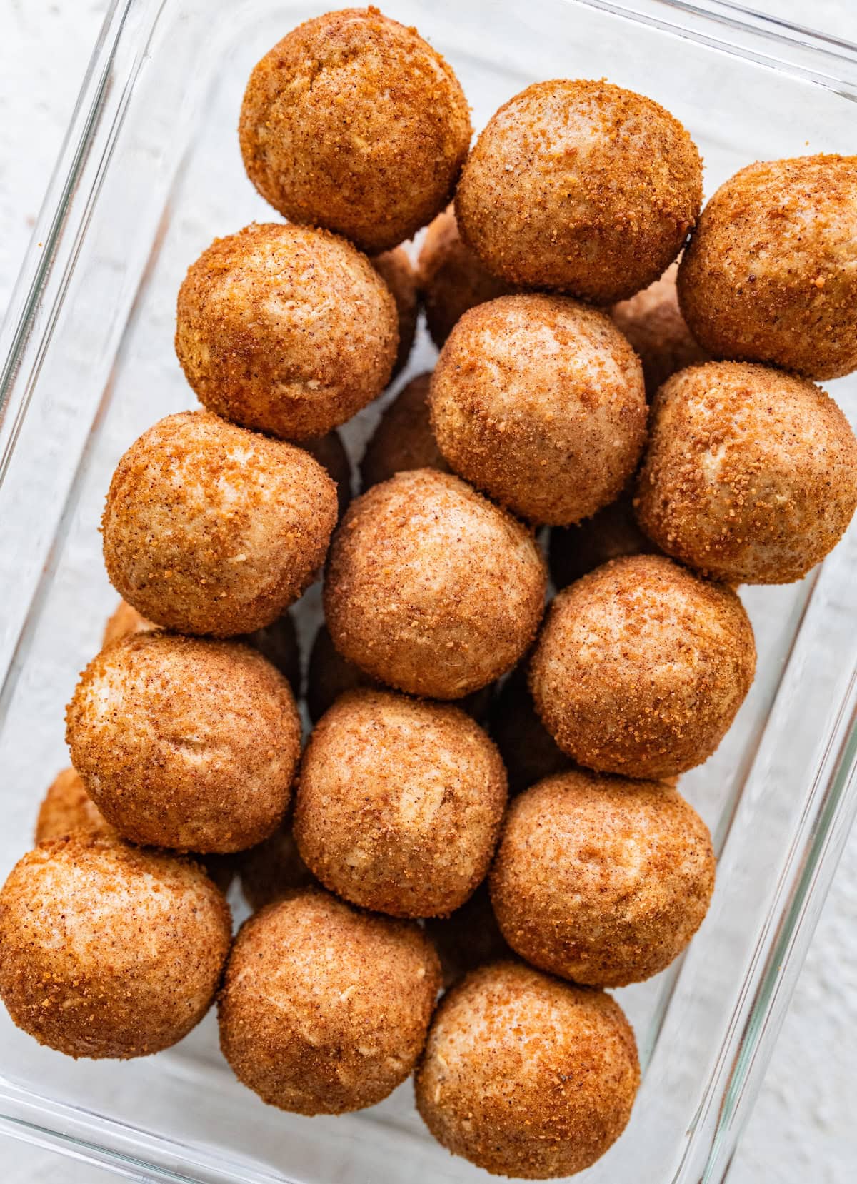Snickerdoodle protein balls packed in a glass container, showing their cinnamon sugar coating.