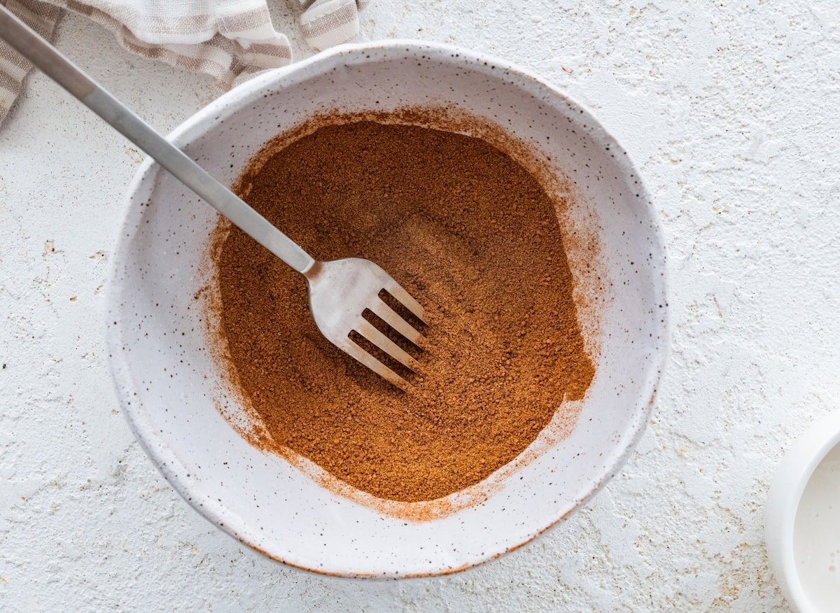 Bowl of cinnamon sugar mixture with a fork ready for coating the protein balls.