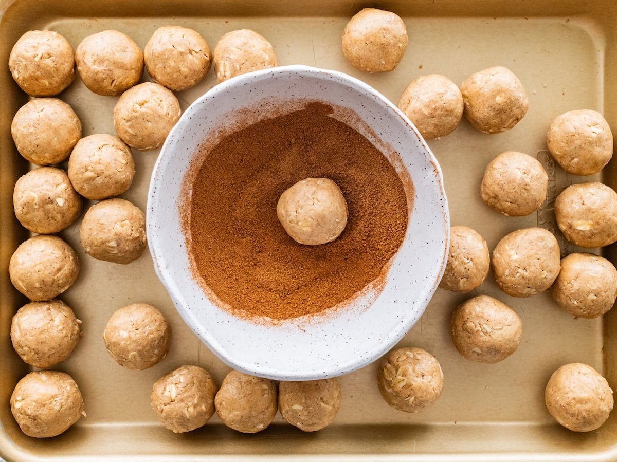 Protein ball being rolled in a cinnamon sugar mixture on a sheet pan with more balls around.