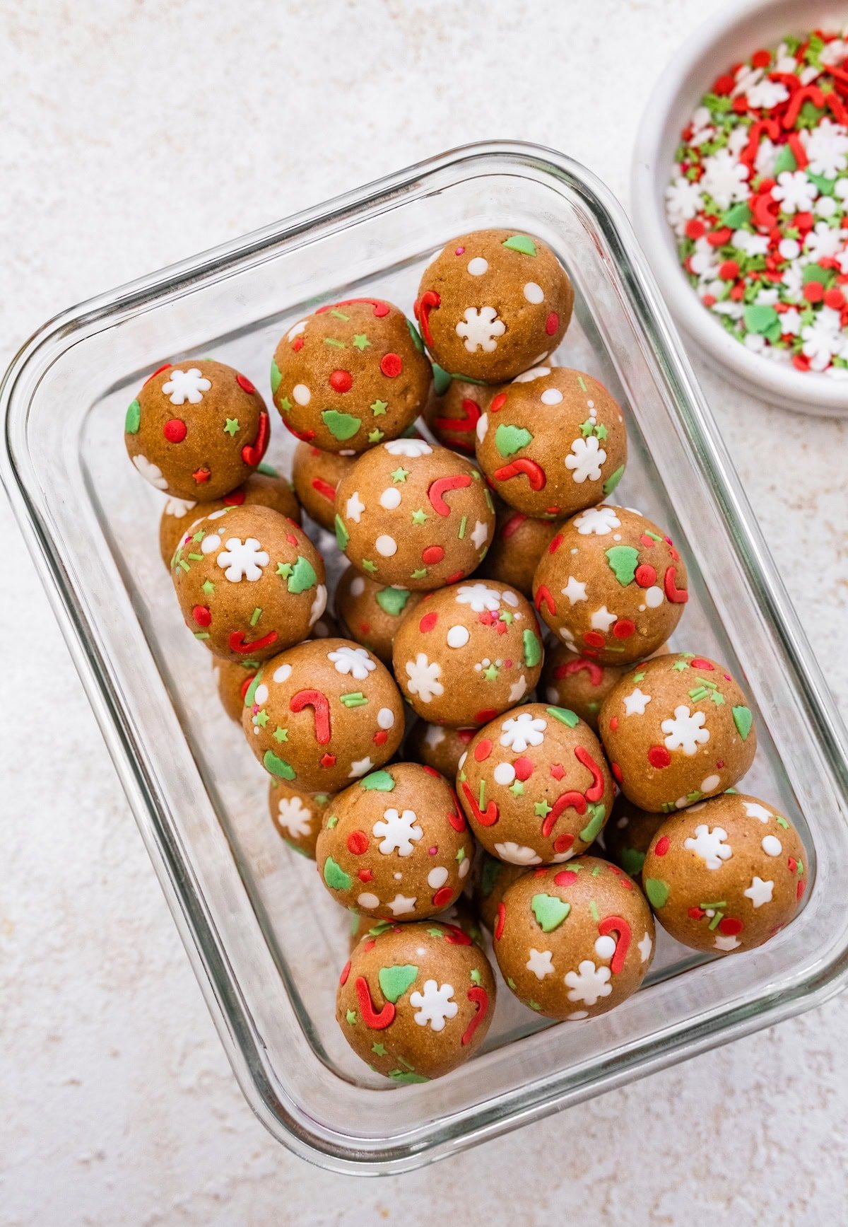 A glass storage container filled with sugar cookie protein balls coated in red, green, and white holiday sprinkles.