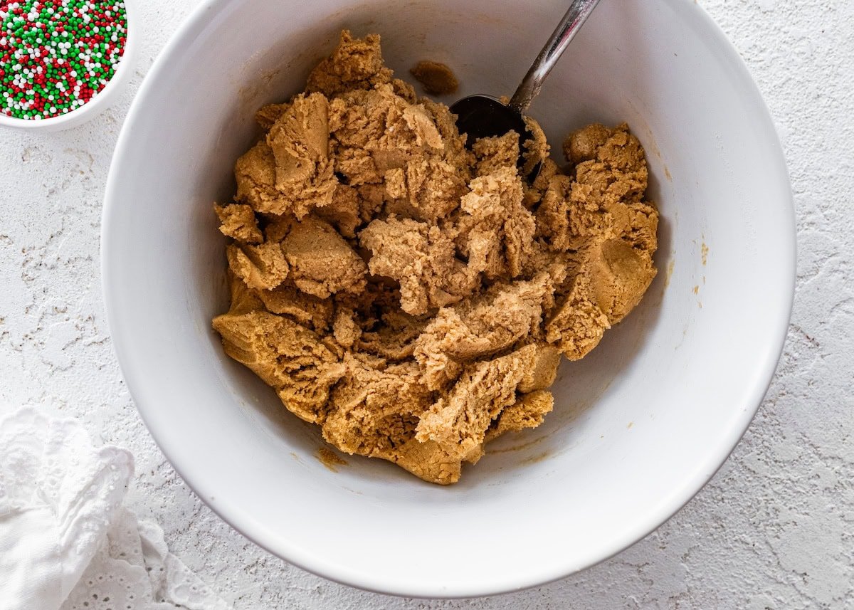 A white mixing bowl filled with thick sugar cookie protein ball dough, ready to be rolled into balls.
