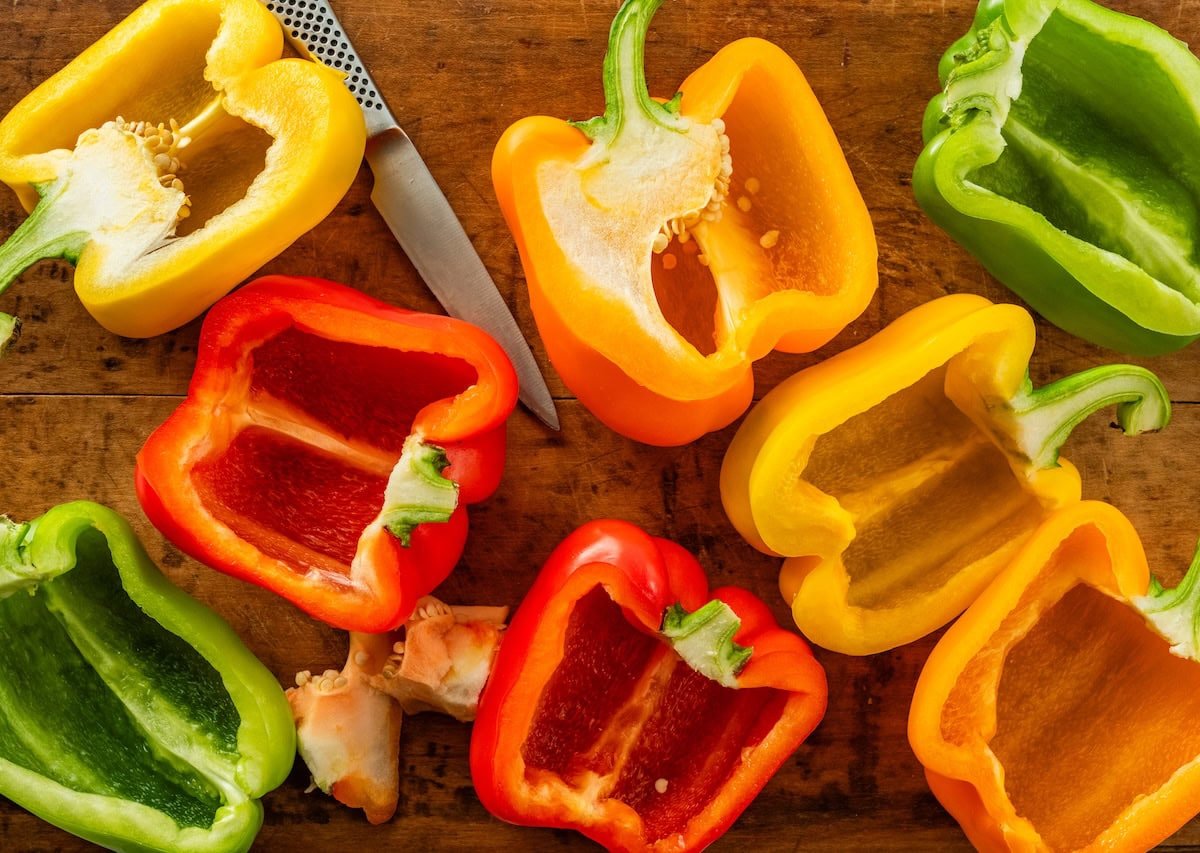 A cutting board with halved yellow, green, and red bell peppers.