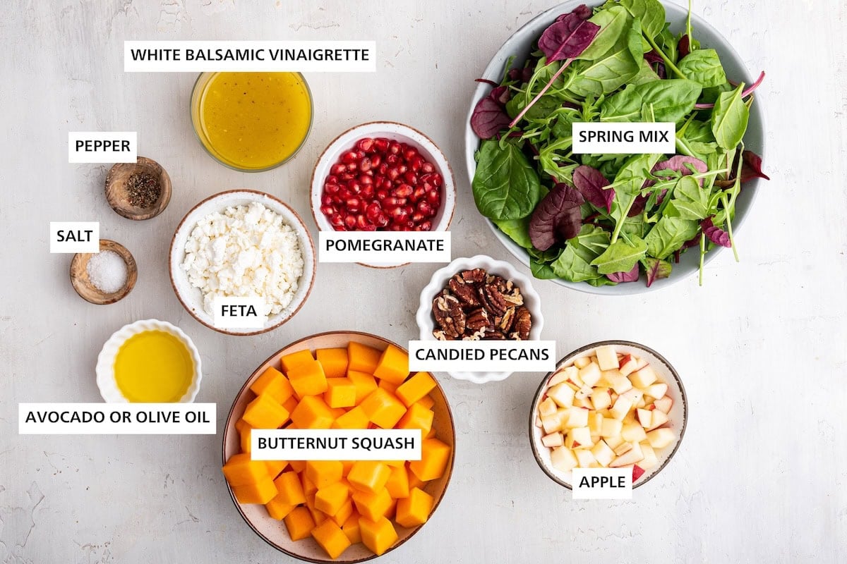 Ingredients measured out to make a Winter Salad: spring mix, candied pecans, apple, pomegranate, butternut squash, white balsamic vinaigrette, feta, pepper, salt and olive oil.
