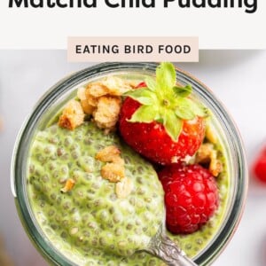 Close-up of matcha chia pudding in a jar topped with strawberries, raspberries, and granola with a spoon.