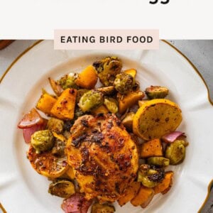 Plated roasted chicken thigh with sweet potatoes, Brussels sprouts, red onion, and roasted lemon on a white plate.