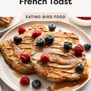 Two slices of protein French toast topped with blueberries and raspberries, drizzled with syrup and nut butter on a plate.