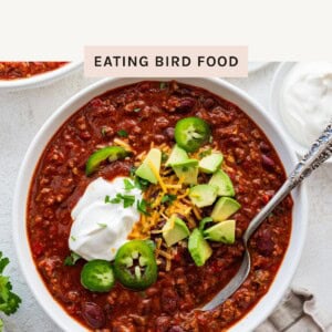 Bowl of slow cooker chili topped with sour cream, sliced jalapeños, avocado, and shredded cheese.