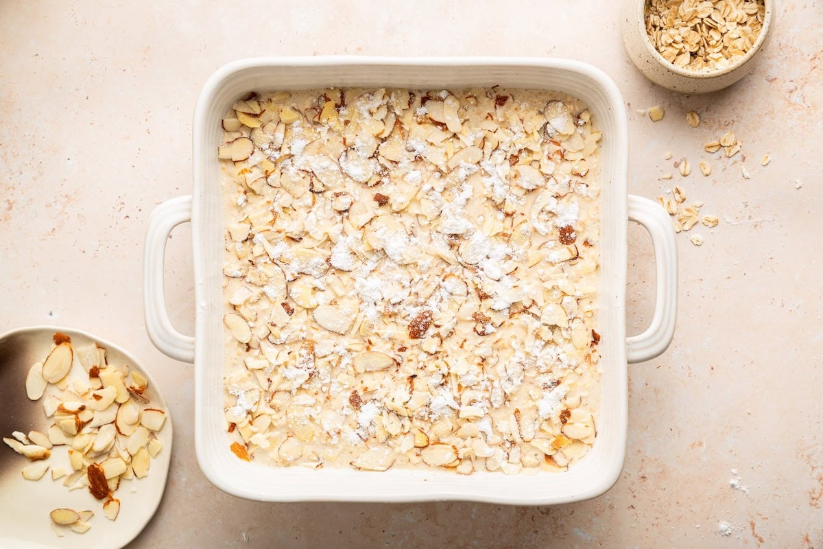 Unbaked almond croissant baked oatmeal with sliced almonds in baking dish.