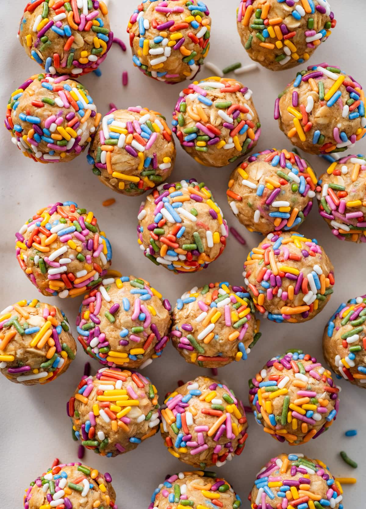 Birthday cake protein balls with colorful sprinkles spread out on a counter top.
