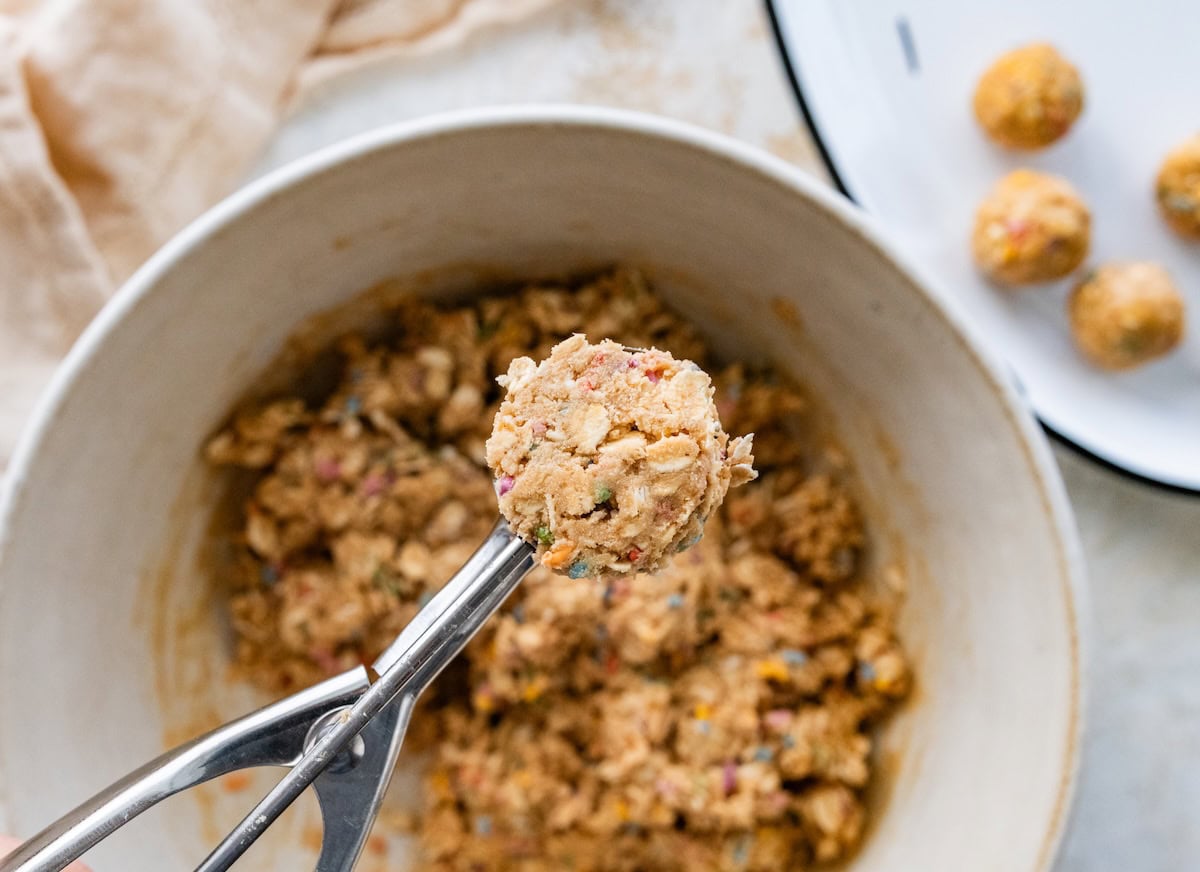 A small cookie scoop forming birthday cake protein balls.