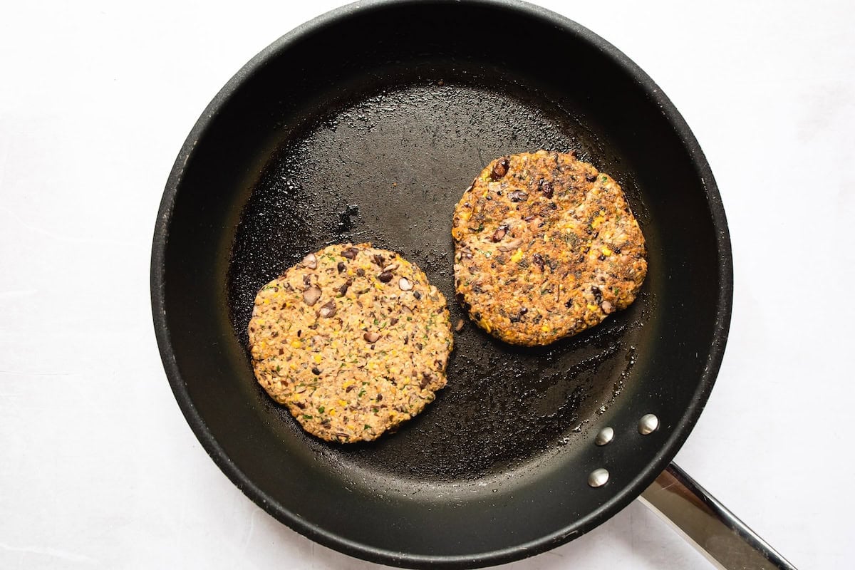 Black bean burger patties being cooking in a black skillet.