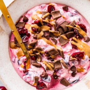 Spoon stirring chocolate cherry cheesecake yogurt bowl.