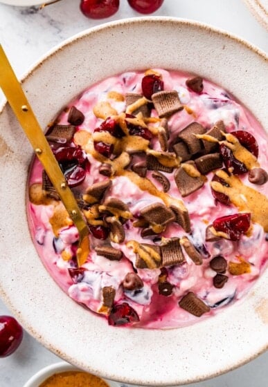Spoon stirring chocolate cherry cheesecake yogurt bowl.