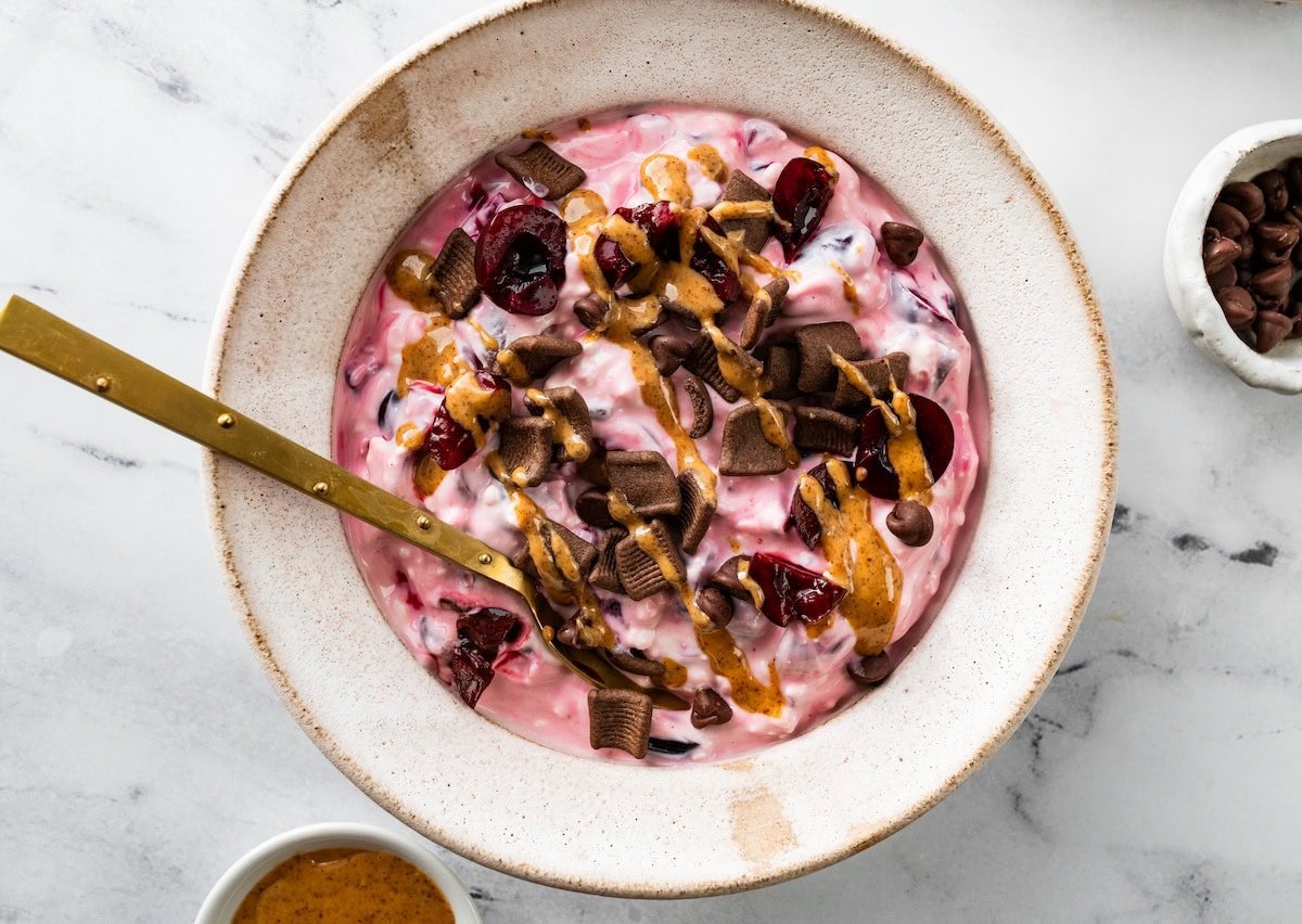 Chocolate cherry cheesecake yogurt bowl with chocolate chips and almond butter drizzle.