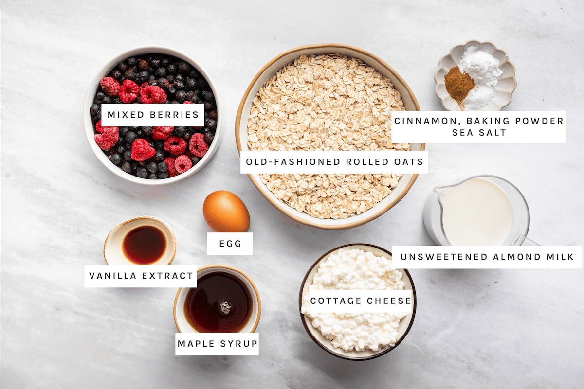 Ingredients for cottage cheese baked oatmeal cups: mixed berries, rolled oats, vanilla, maple syrup, egg, cottage cheese, almond milk, cinnamon, baking powder and salt.