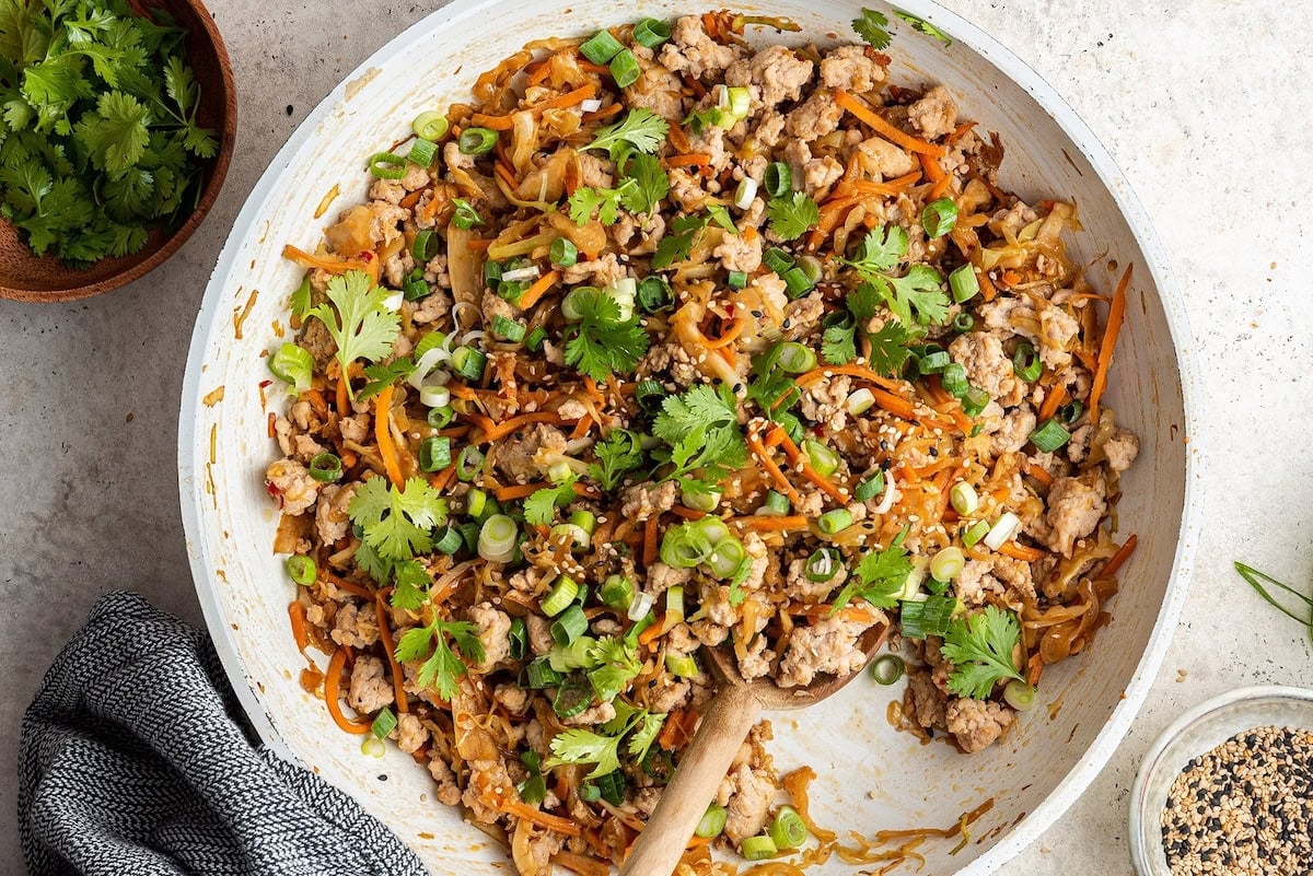 A skillet containing egg roll in a bowl. A wooden serving spoon rests in the pan.